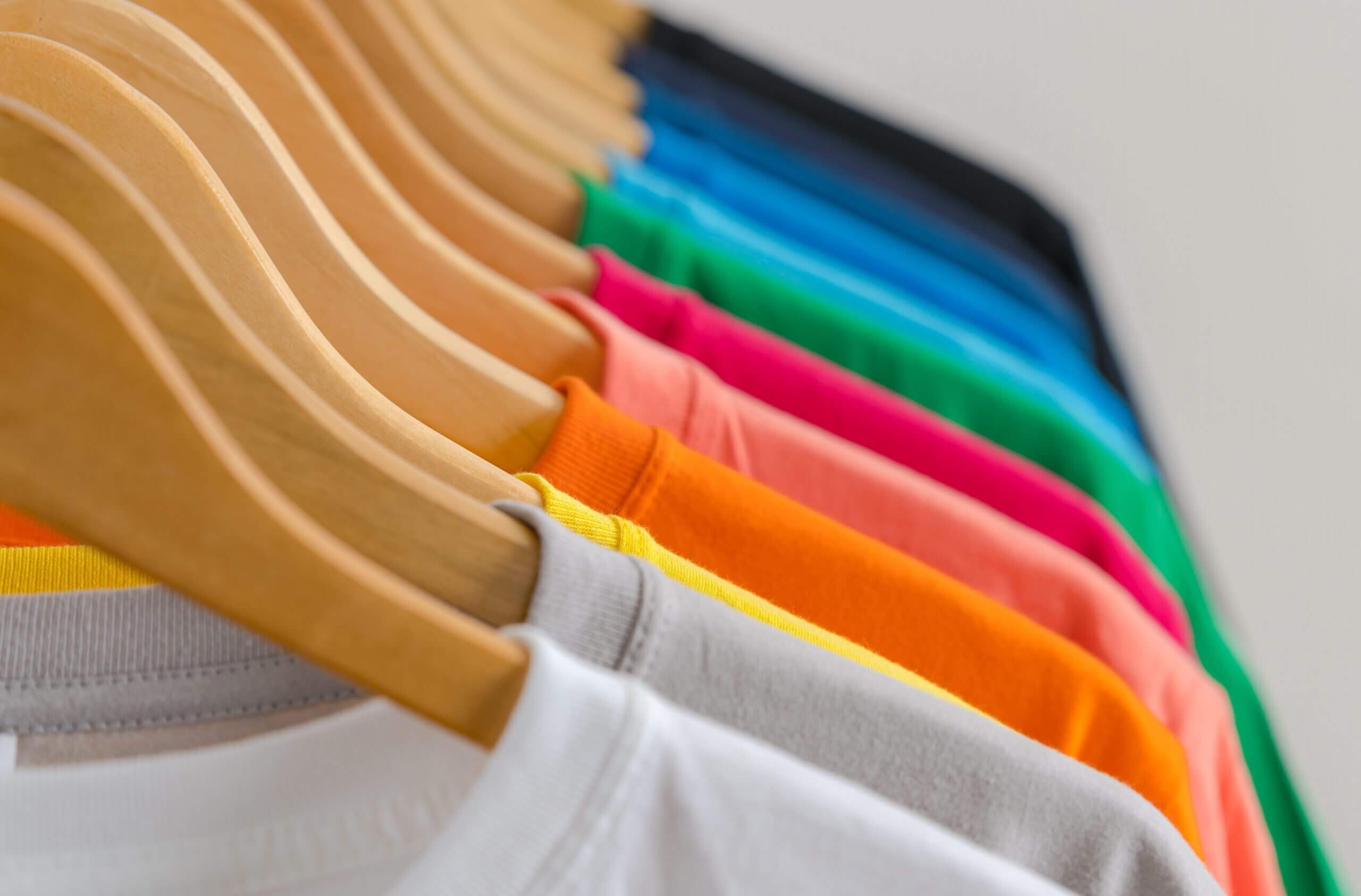 A row of different colored shirts hanging on hangers.