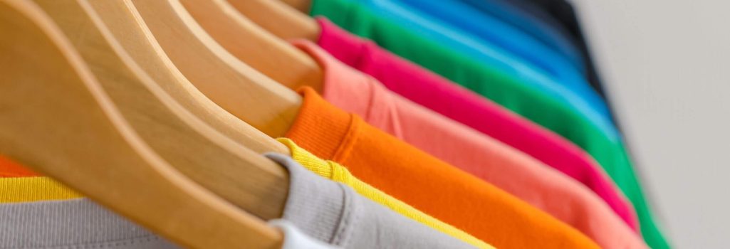 A row of different colored shirts hanging on hangers.